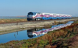 An Altamont Corridor Express train operating along the San Francisco Bay; a MPI F40PH-2C locomotive hauls a consist of Bombardier BiLevel Coaches.