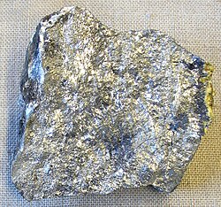 An irregular piece of silvery stone with spots of variation in luster and shade