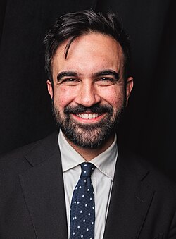 Mayor Zohran Mamdani wearing a black suit and smiling