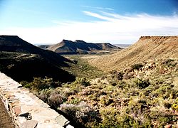 A view from the top of the Great Escarpment in the Karoo National Park near Beaufort West, looking south across the plains of the Lower Karoo: Note the remnants and extent of the former central plateau on the plain below the escarpment (see diagram on the right). Also note the dolerite sills which top the escarpment and mountains in the middle distance, giving these structures their characteristic flat-topped appearance.