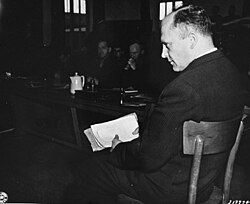 Priest Friedrich Hoffman testifies at the trial of former camp personnel and prisoners from Dachau. In his hand he holds records showing that hundreds of priests died at the camp after being exposed to malaria during Nazi medical experiments.