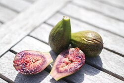 Two whole figs and two sliced fig halves on a wooden table in natural light