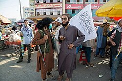 Taliban fighters at a market in Kabul, September 2021. A vendor selling Islamic Emirate flags can be seen.