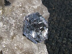Lustrous, silvery, flat, hexagonal crystals in roughly parallel layers sit flowerlike on a rough, translucent crystalline piece of quartz.
