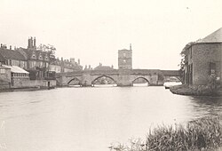 Photograph of an arched bridge over the river, with a rectangular chapel building in the centre