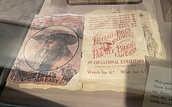 Color image showing two white men in cowboy hats, the Bills, next to a yellowing brochure printed with red ink, which lists cities and dates where the show will be.