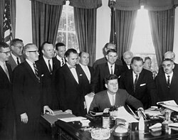 President Kennedy signs the act establishing the United States Travel Service, 29 Jun 1961 in the presence of Manolita Doelger, chairwoman of ETC New York (third from the right).