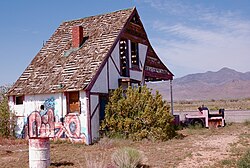 Rear view of the Santa Claus Land Sales Office looking northeast, 2008. To the right is the "Old 1225", a derailed, pink children's train tagged with graffiti. U.S. Route 93, Ithaca Peak (left), and Turquoise Mountain (right) can be seen in the background.