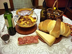 Table with typical Italian dishes: red wine, tortelli with meat sauce, salami, Parmesan cheese, and colonial bread