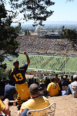 Fans atop Tightwad Hill watch the Cal Band, with views of the stadium and the San Francisco Bay.