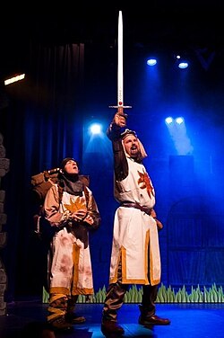 King Arthur (holding Excalibur) and Patsy in Spamalot, a stage musical adaptation of the 1975 comedy film Monty Python and the Holy Grail