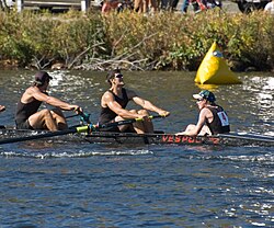 A coxswain (far right) sitting in the stern of the boat, facing the rowers, at the Head of the Charles Regatta.