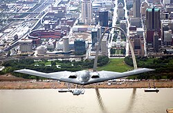 B-2 in flight over the Mississippi River (St. Louis, Missouri) with the Gateway Arch, St. Louis Basilica, and Busch Stadium and footprint of Busch Memorial Stadium in the background