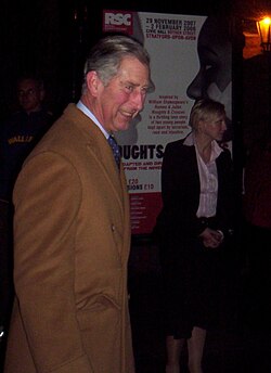 Charles in a brown coat attending the performance in Stratford-upon-Avon