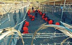 Captives at Camp X-Ray, Guantanamo Bay, Cuba, a United States military prison where people are being indefinitely detained in solitary confinement as part of the "war on terror" (January 2002). The prisoners are forced to wear goggles and headphones for sensory deprivation and to prevent them from communicating with other prisoners.