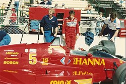 Mario Andretti waits by his car during a practice session at the 1987 Indianapolis 500.