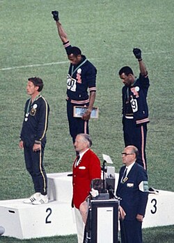 Gold medallist Tommie Smith (centre) and bronze medallist John Carlos (right) showing the raised fist on the podium after the 200 m race at the 1968 Summer Olympics; both are wearing Olympic Project for Human Rights badges. Peter Norman (silver medallist, left) from Australia is also wearing an OPHR badge, in solidarity with Smith and Carlos.