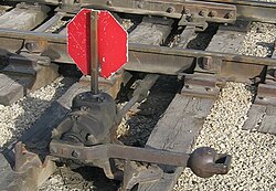 An example of a mechanism used at a switch. The two points are linked together with a throw bar (also known as a stretcher bar). The throw bar extends to the lever on the near side of the track, which is used to throw the switch. This is an example of a low switch stand, used at locations where there is not sufficient clearance for a tall switch stand. This particular stand is designed to be trailed through by rolling stock, which will cause the points to become lined for the route that the wheels have passed through. It has a reflectorized target.
