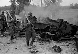 Finnish troops equipped with Panzerfaust antitank weapons walk past a destroyed Soviet T-34 tank during the Battle of Tali-Ihantala. The lead soldier is also armed with a Suomi KP/-31.