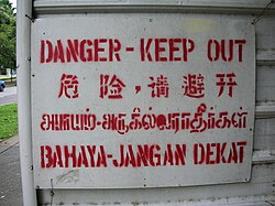A stenciled danger sign in Singapore written in English, Mandarin, Tamil, and Malay (the four official languages of Singapore)