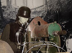 A model of a typical entrenched German machine gunner in World War I. He is operating an MG 08, wearing a Stahlhelm and cuirass to protect him from shell fragments, and protected by rows of barbed wire and sandbags.