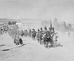 A photograph showing a regiment of Indian cavalry riding their horses in a column through Damascus