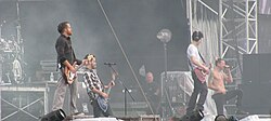A color photograph of members of the group Linkin Park performing on and outdoor stage