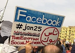 A man during the 2011 Egyptian protests carrying a card saying "Facebook,#jan25, The Egyptian Social Network"