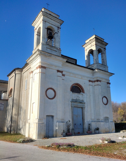 An off white, cube shaped building, with stepped trim and two small bell towers on the front corners of the roof.