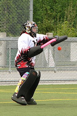 A goalkeeper makes a glove save. Equipment worn here is typical gear for a field hockey goalkeeper.
