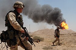 A U.S. soldier stands guard duty near a burning oil well in the Rumaila oil field, 2 April 2003