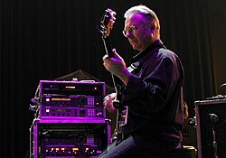 Robert Fripp ergonomically plays electric guitar while sitting in a posture developed through years of application of the Alexander Technique.