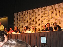 A long table with a group of white men sitting behind it, each with a microphone in front of them