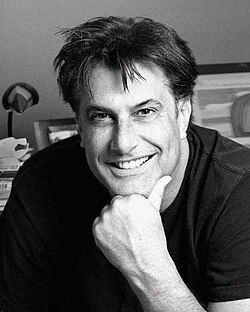 A man with straight black hair smiles as his chin lays on his fist, with the portrait taken at a studio.