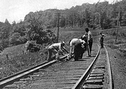 Circa 1917, an American section gang (gandy dancers) responsible for maintenance of a particular section of railway. One man is holding a lining bar (gandy), while others are using rail tongs to position a rail. Superelevation (cant) is clearly evident on the curve.