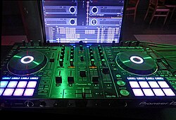 Pioneer DDJ-RX controller with the mixing software rekordbox running on a computer. The physical setup (two "discs" as primary tools, mixing controls mainly in the middle) of this digital DJ workplace strongly resembles the style of the old analog DJ set above, as the latter was standard and "best practice".