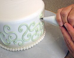Buttercream swirls being piped onto the sides of a cake with a pastry bag