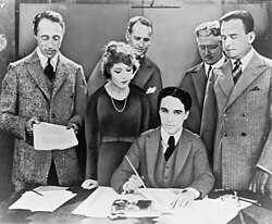 Griffith, Pickford, Chaplin (seated), and Fairbanks at the signing of the contract establishing the United Artists motion-picture studio in 1919.Lawyers Albert Banzhaf (left)and Dennis F. O'Brien (right)stand in the background.