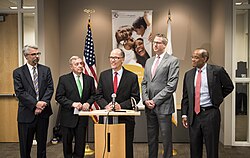 Secretary of Labor Thomas Perez (center) speaks at a press conference at Chicago's Center for Economic Progress. Rogers is on the far right.