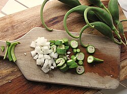 Unripe pods of Proboscidea parviflora chopped with onions on a cutting board.