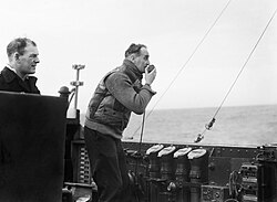 Walker using a loud hailer to encourage one of the ships under his command during an attack on a submarine in early 1944