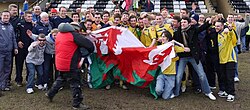 A TV cameraman records Barry fans and players celebrating after their Welsh Cup Quarter Final win at Flint Town United on 2 March 2013.