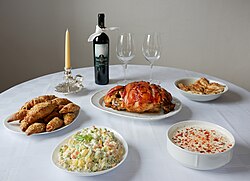 The traditional Serbian Christmas table features roast pork, hearty soup, crescent rolls, and Olivier salad, accompanied by wine or rakija.