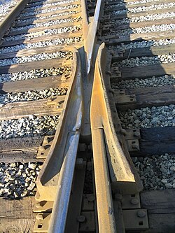 A one-piece cast crossing. The shiny line crosses the rusty line. This North American "self-guarding cast manganese" component without guard rails has raised flanges on the crossing, which may bear on the face of the wheel as it passes through.