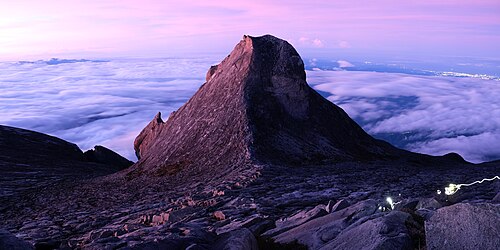 Climbers ascending toward Low's Peak before sunrise on Mount Kinabalu, with the distant city lights of Kota Kinabalu visible far right, Sabah, Borneo