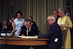 Johnson signs the Social Security Amendments of 1965 while seated next to former President Harry S. Truman