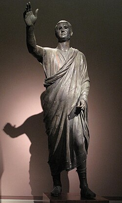 The Orator, c. 100 BC, an Etrusco-Roman statue of a Republican senator, wearing toga praetexta and senatorial shoes; compared to the voluminous, costly, impractical togas of the Imperial era, the Republican-era type is frugal and "skimpy" (exigua).[311]