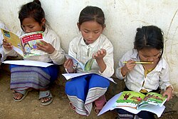 Three Laotian girls sit outside their school reading.