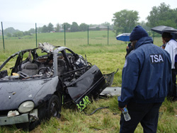TSA officers view the post-blast remains of a Dodge Neon after an explosive was detonated inside it during training.