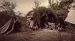 Chiricahua medicine man in wickiup with family